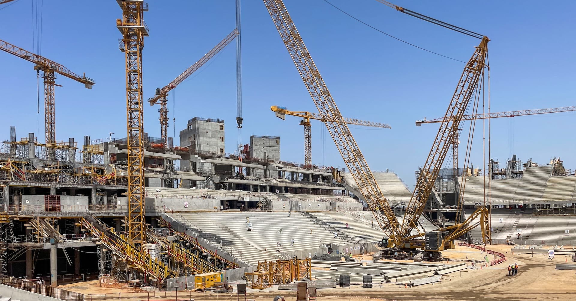 Construction workers at the massive Hassan II Stadium site in Benslimane near Casablanca, with steel structures rising against the skyline.