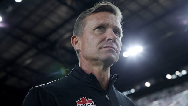 Jesse Marsch, wearing a Canada Soccer training top, stands on the sideline with a focused expression during a match.