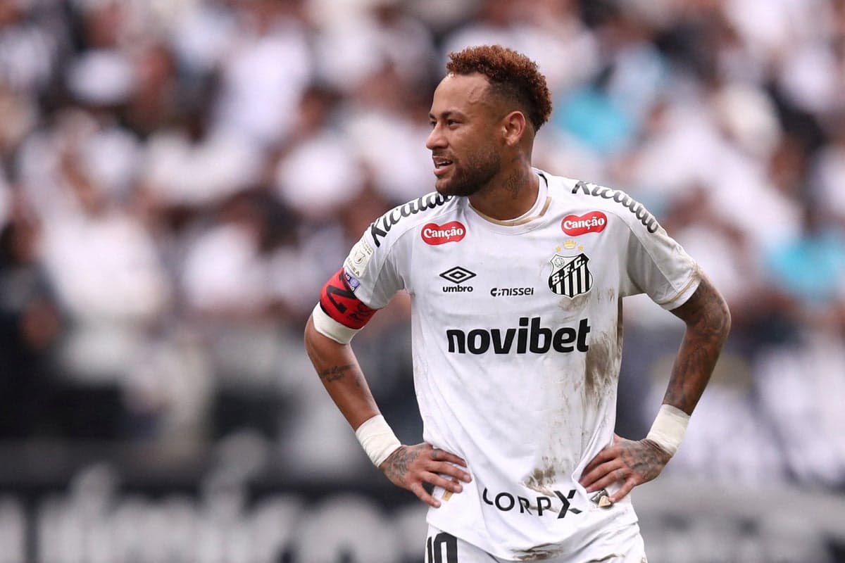 Neymar sitting on the pitch holding his right calf, wearing a Santos FC kit during a BrasileirĂŁo match, visibly grimacing in pain.