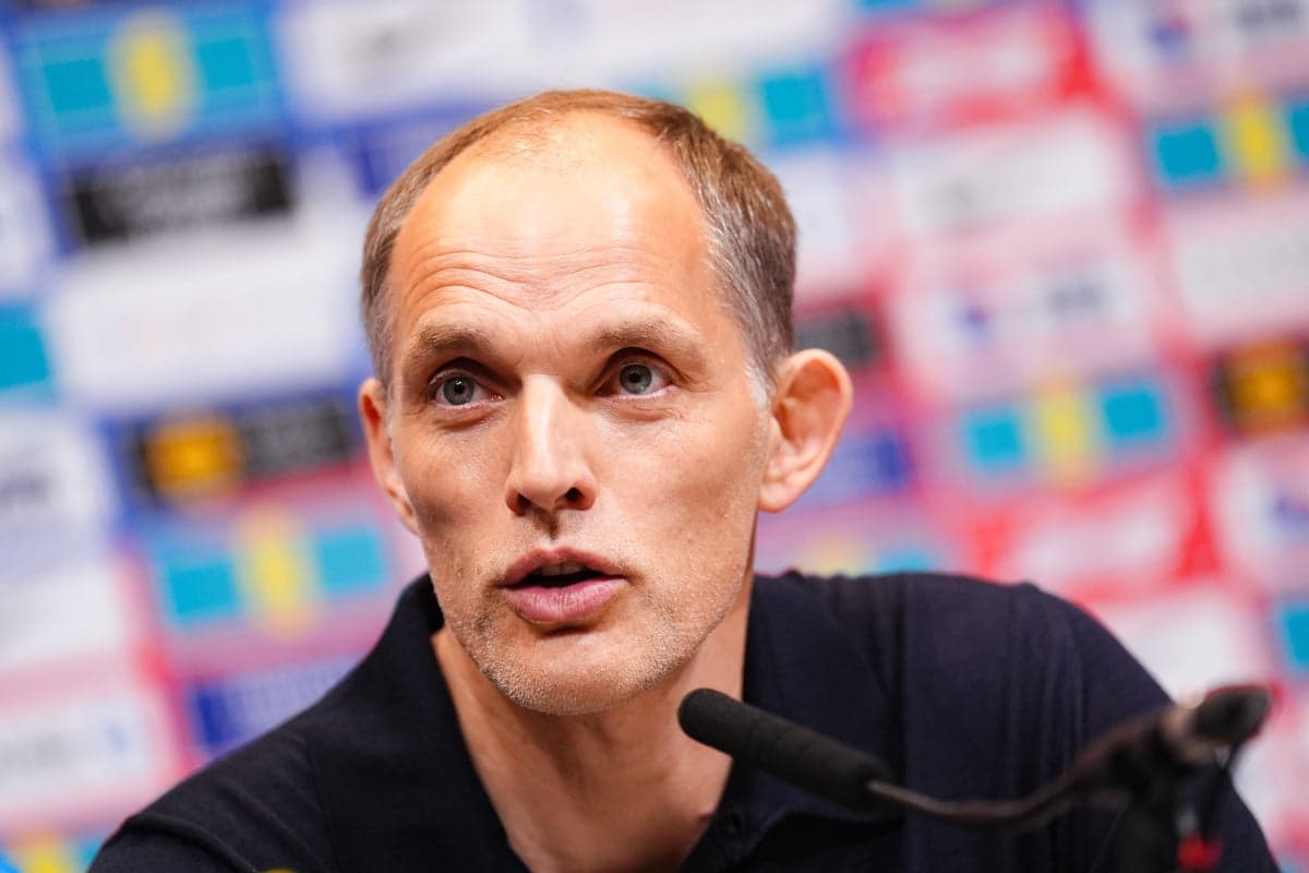 Thomas Tuchel standing beside a white tactical board with the England squad logo and a list of World Cup 2026 group fixtures displayed beside it.